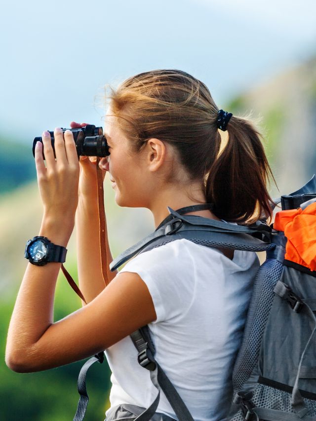 woman using binoculars with backpack on