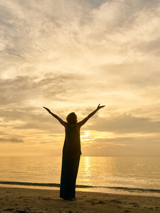 woman with arms up in front of the sunset on the beach