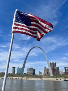 An American flag flies in front of the Gateway Arch, an iconic landmark in St. Louis.
