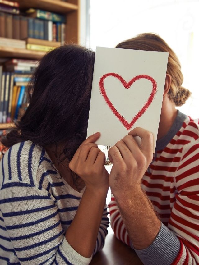 a couple with a piece of paper with a heart on it covering their faces