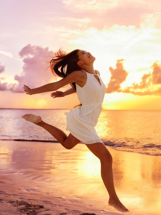 girl jumping on the beach in a white dress during the sunset