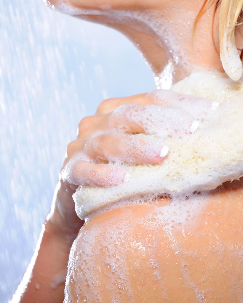 best body wash before spray tan woman showering using a loofa and body wash