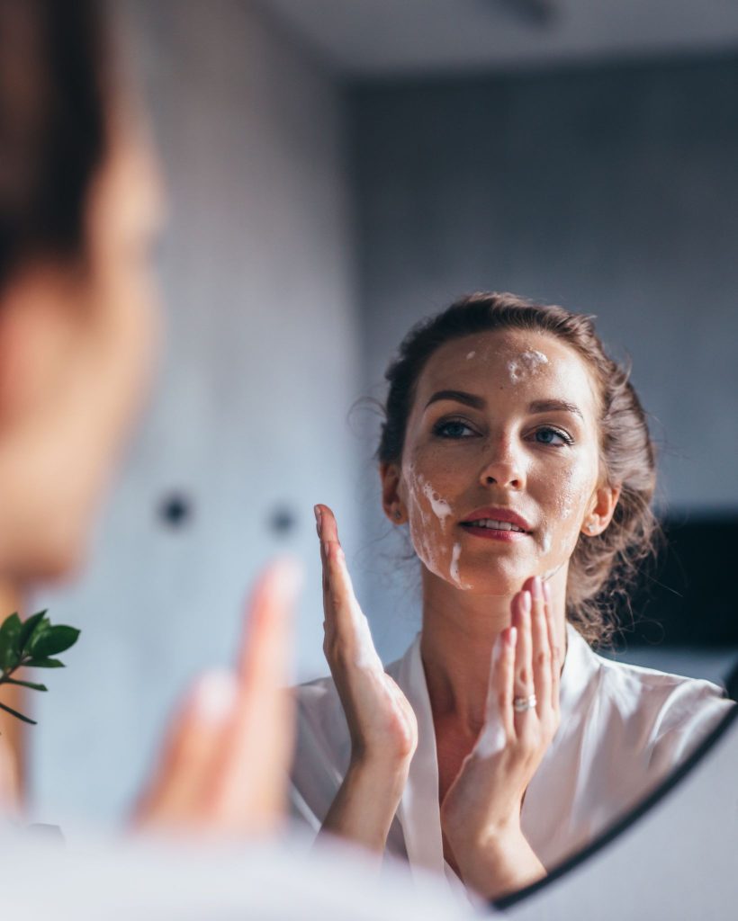 Woman applying moisturizer to her face in the mirror
