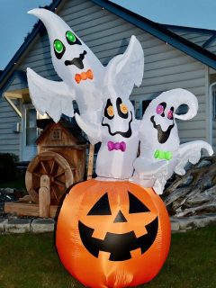 Three inflatable ghosts on a pumpkin in front of a house, the best halloween inflatables for spooky home decor.