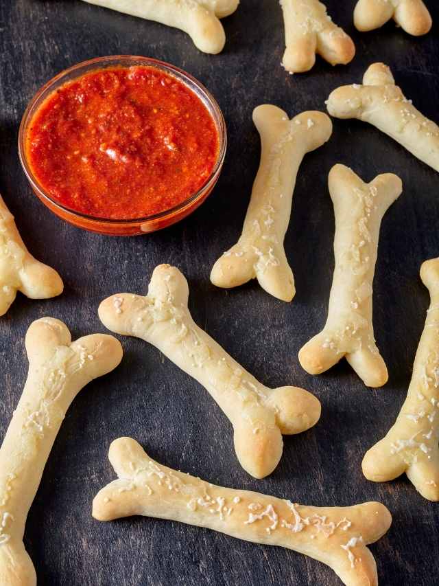 A tray of dog bone shaped bread sticks with a dipping sauce.