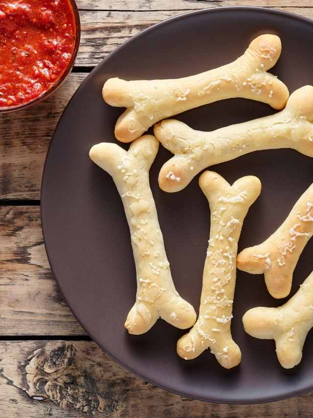 A plate of dog bone shaped bread sticks on a wooden table.