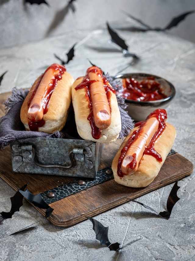 Three hot dogs on a tray with ketchup and bats.