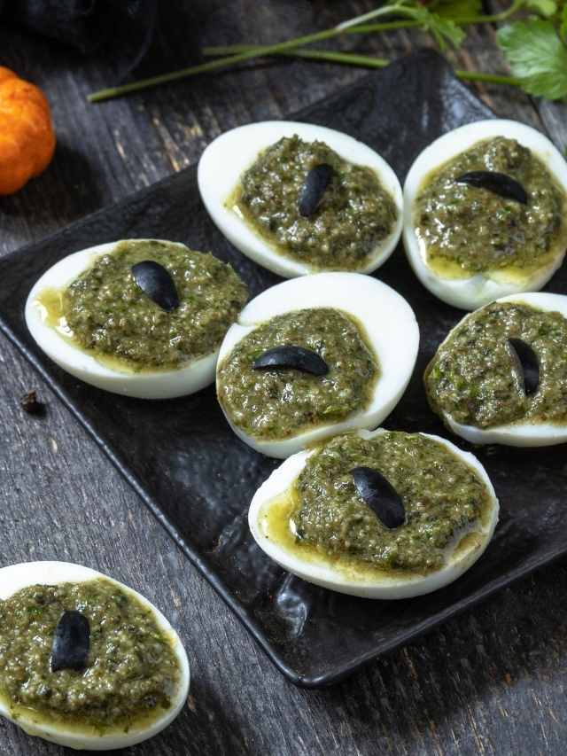 Deviled eggs with pesto on a black plate.