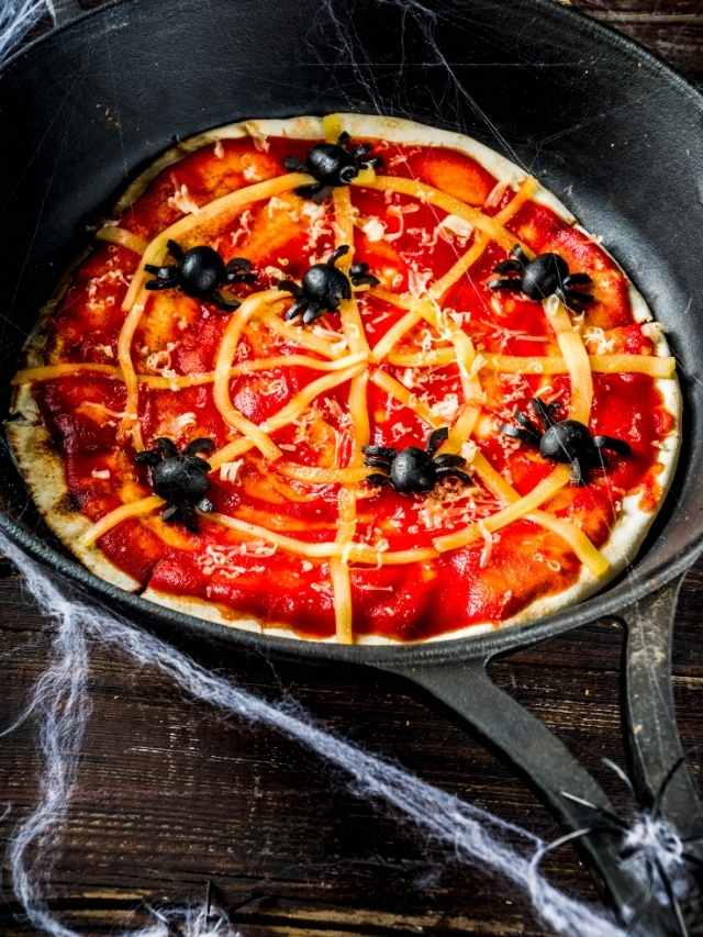 A halloween pizza in a skillet with spiders and spider webs.