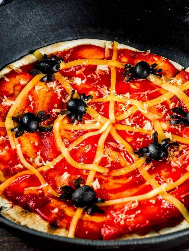 A pizza in a skillet with black spiders on it.
