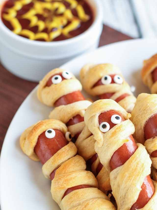 Mummy hot dogs on a plate with dipping sauce.
