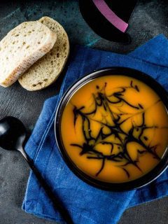 A bowl of pumpkin soup with bread on a blue cloth.