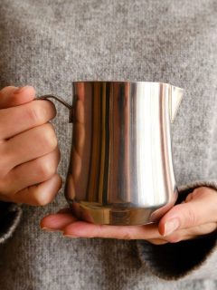 A woman holding a stainless steel milk jug.