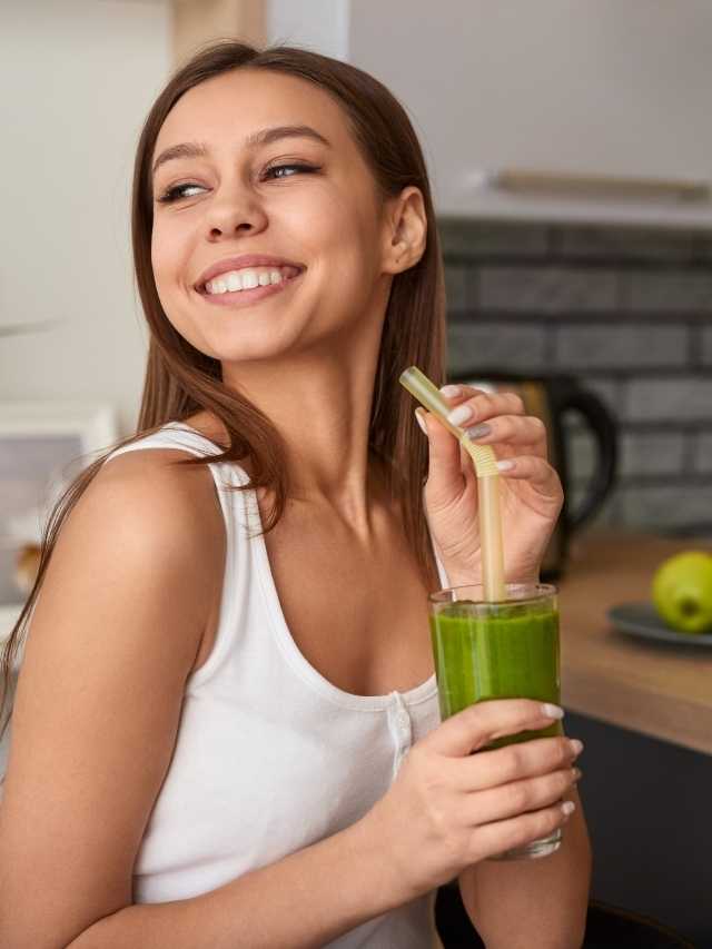 A woman holding a glass of green juice.