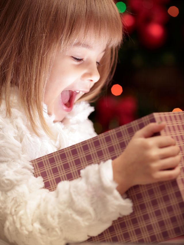 A little girl is opening a christmas present.