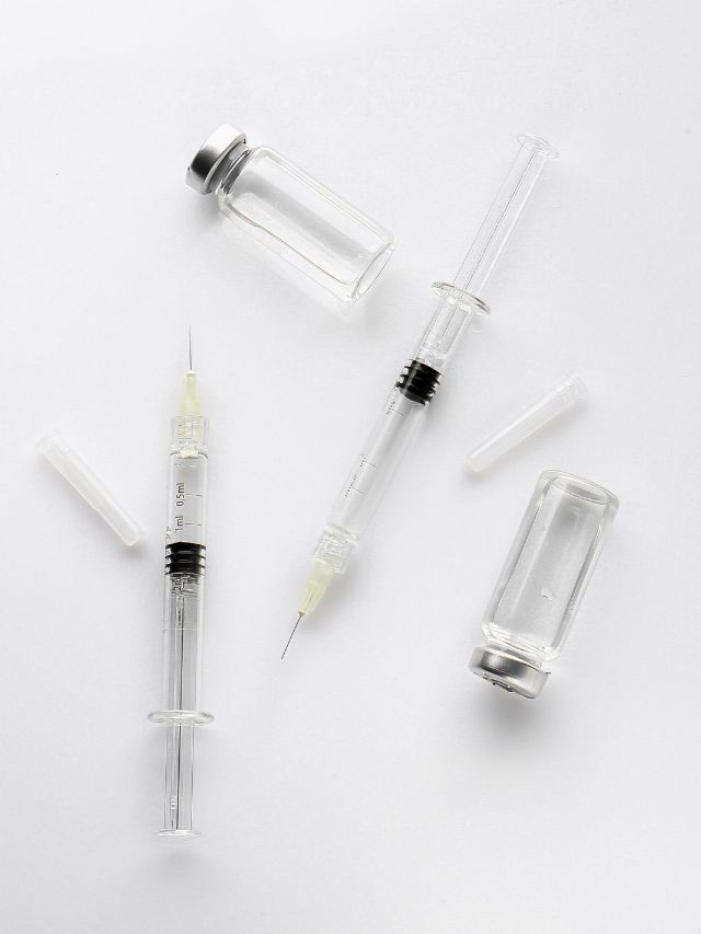 Syringes and needles for facial fillers displayed on a white surface.