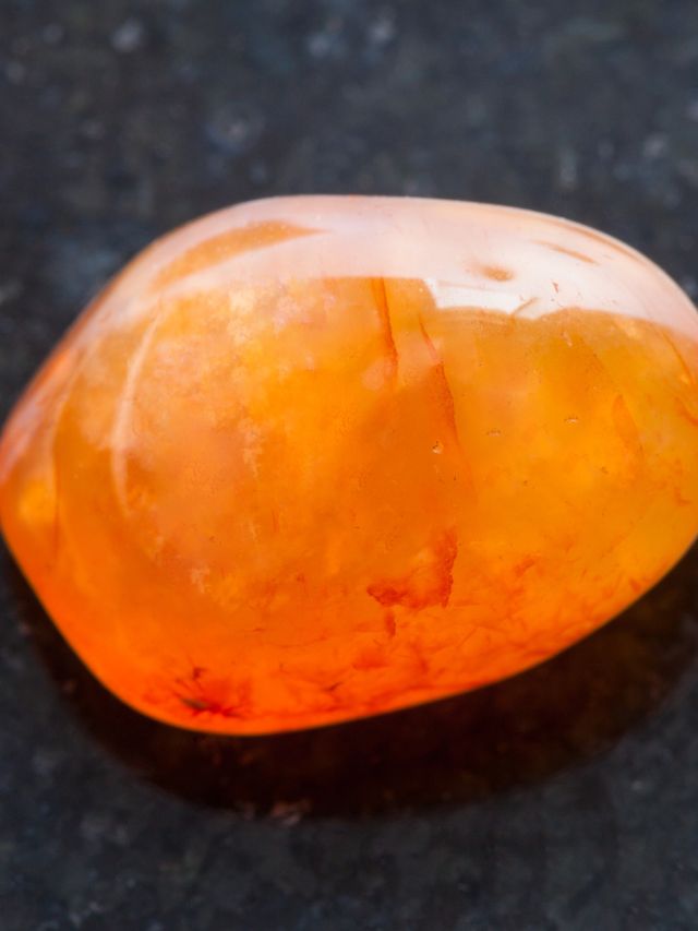 A piece of orange quartz on a black surface.