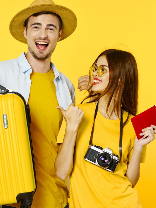 Young couple with luggage and passport on yellow background.