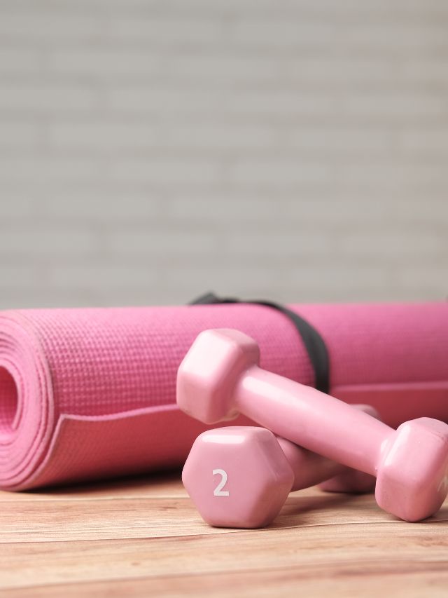 A pink yoga mat and pink dumbbells on a wooden table.