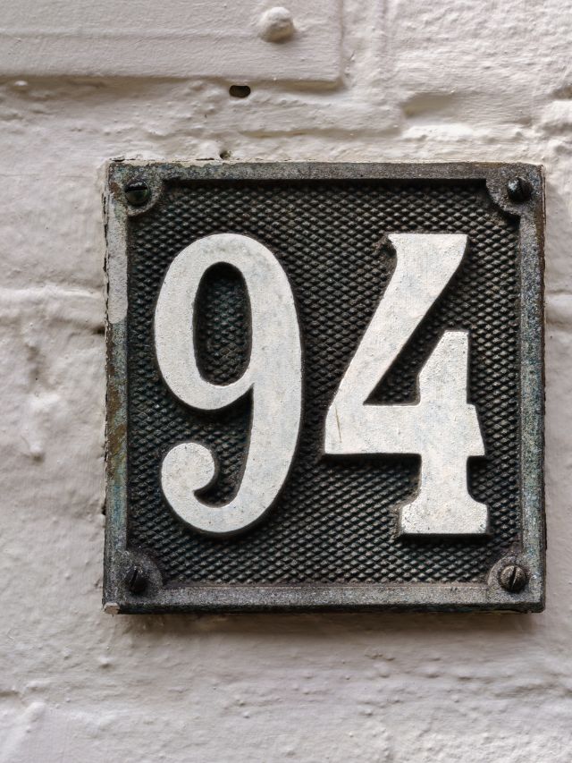A house number sign on a white brick wall with the meaning of spirit number 94.