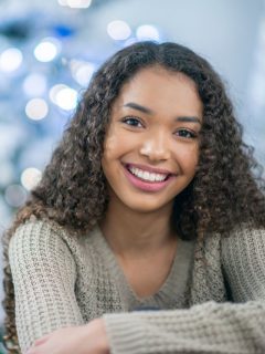 A young African American woman smiling in front of a Christmas tree with cheap Christmas gifts for teens.