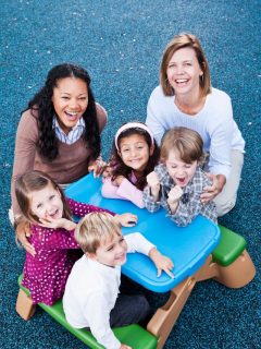A group of children sitting on a blue table in a playground, providing inspiration for Christmas gift ideas for daycare teachers.