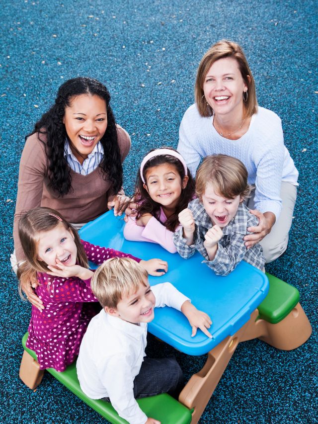 A group of children sitting on a blue table in a playground