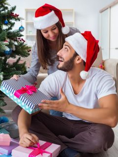 A man and woman in santa hats opening a christmas present.