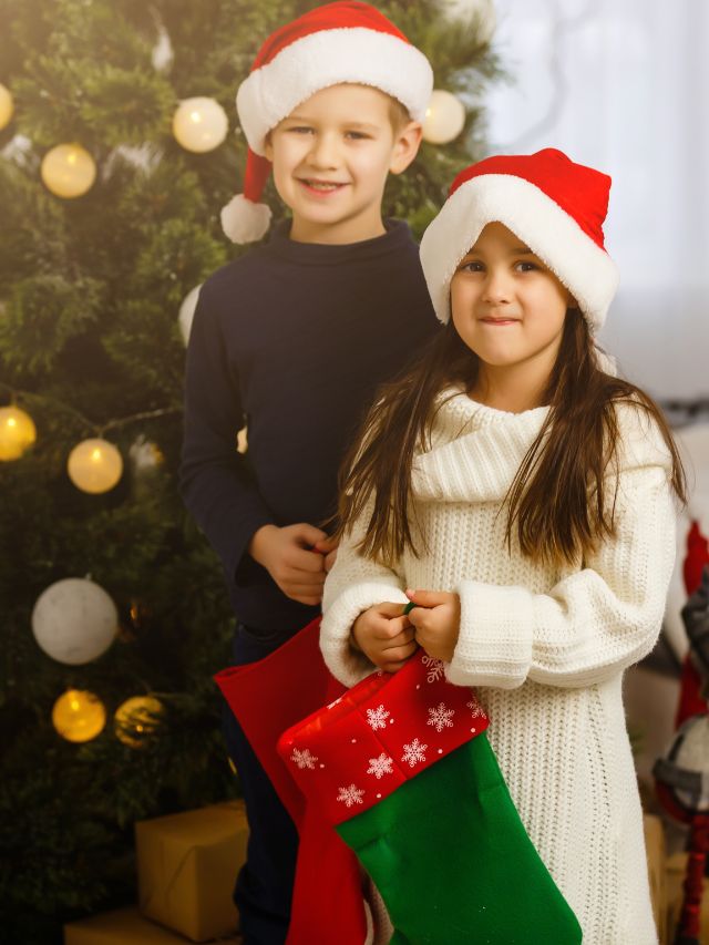 Two children in santa hats standing in front of a christmas tree.