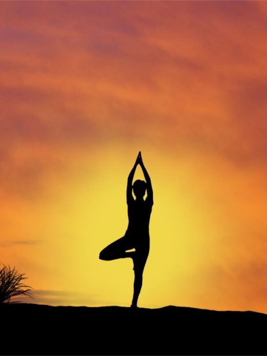 A silhouette of a woman doing yoga at sunset.