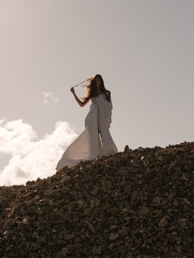 A woman in a white dress standing on a pile of rocks, symbolizing angelic guidance and meaning.