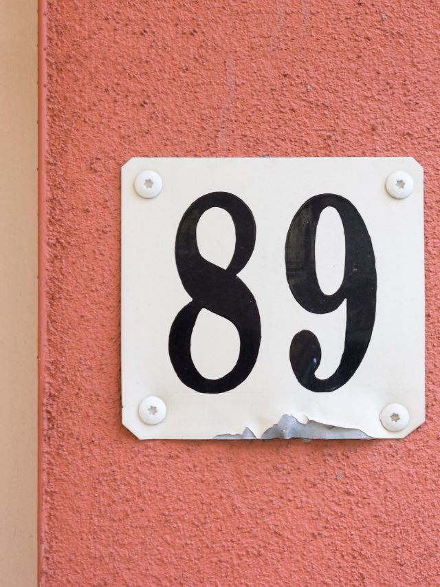 A house number sign on a pink wall with angel number 89 meaning.