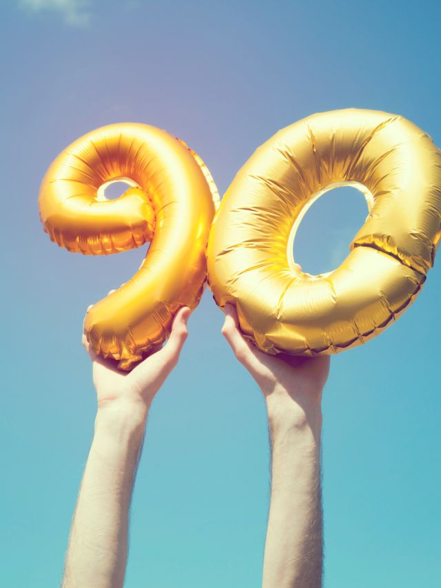 A person holding up a gold balloon with the number 90, symbolizing the meaning of angel number and spirit number.
