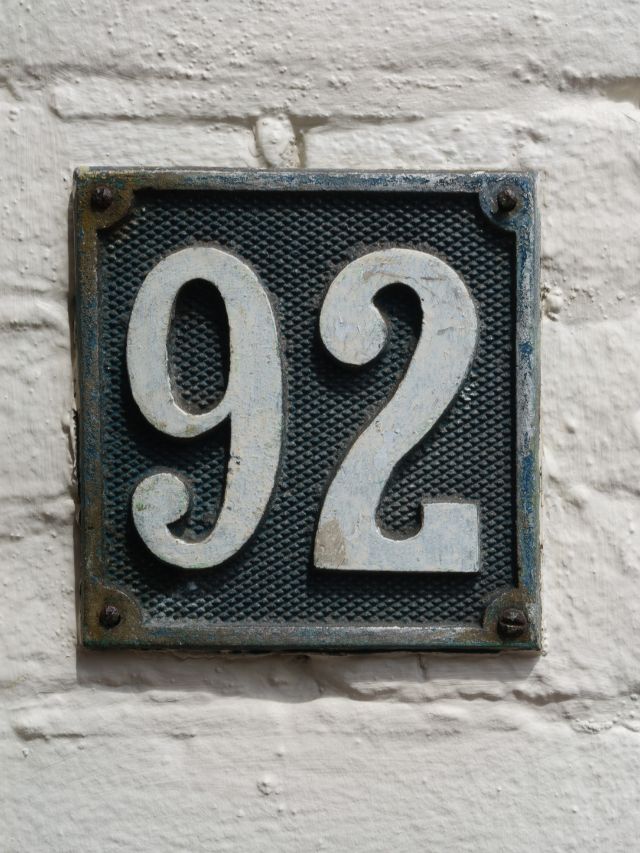A white brick wall with a house number sign depicting the angel number 92.