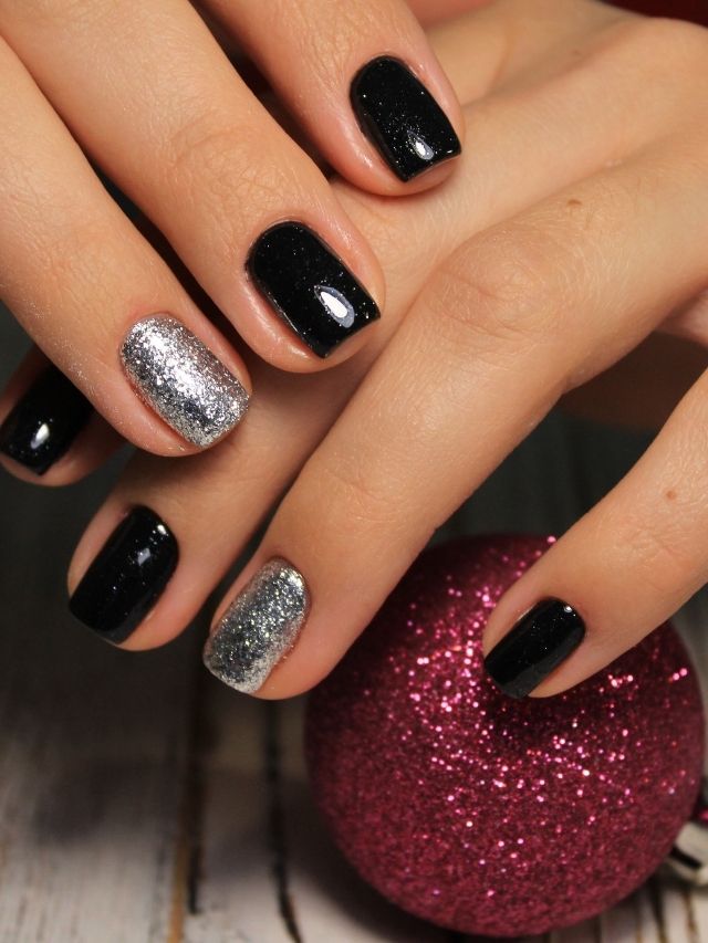 A woman with black and silver nails holding a christmas ornament.