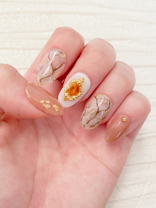 A woman's hand with a gold and beige nail design.