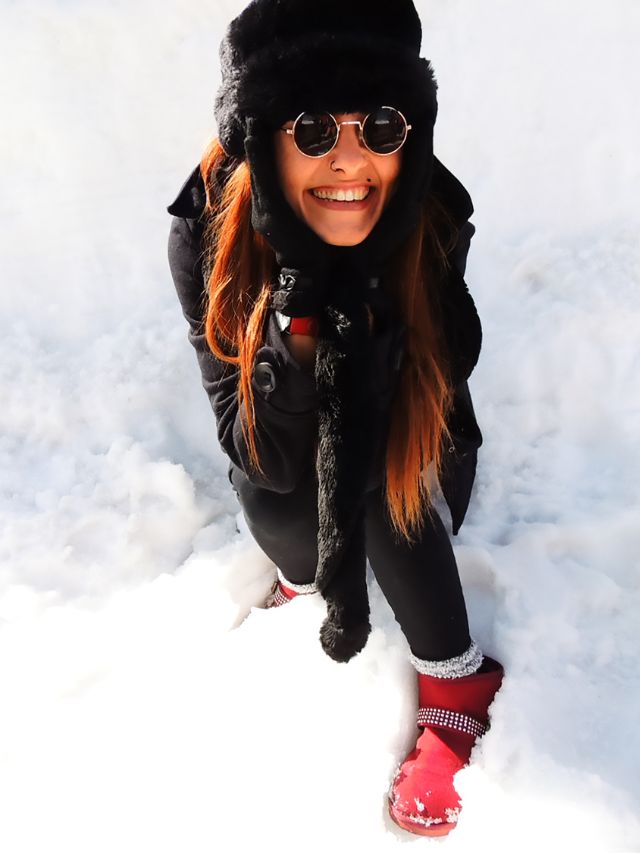A woman wearing sunglasses and a hat is kneeling in the snow.
