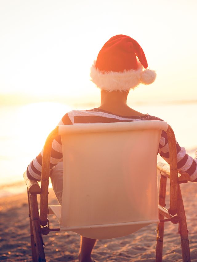 A man in a santa hat sitting in a chair on the beach.