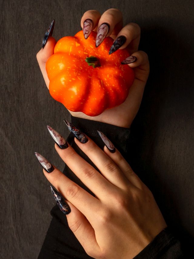 A woman's hand holding a pumpkin with long nails.