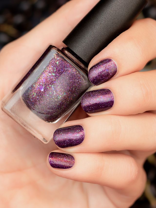 A woman's hand holding a purple nail polish.