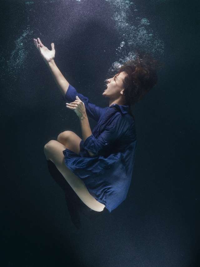 A woman underwater in a blue dress.