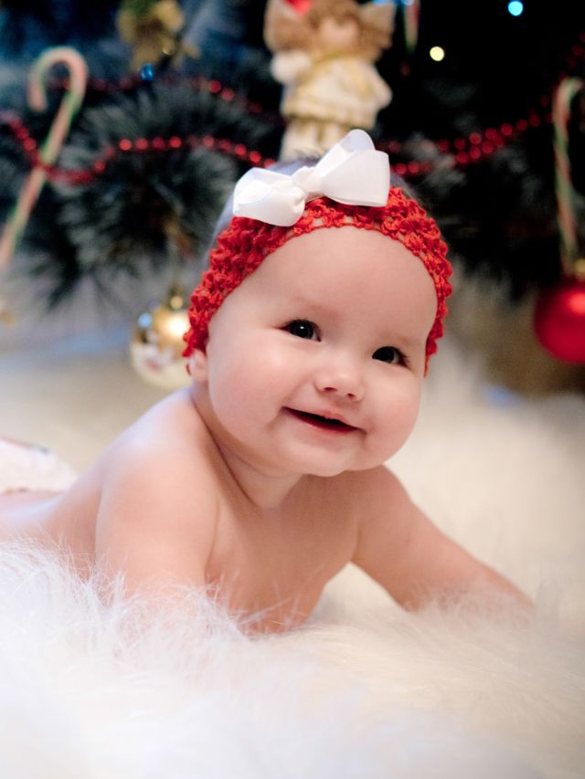 A baby smiles in front of a christmas tree.
