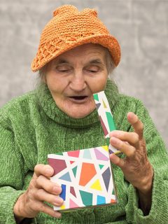 An elderly woman is joyfully holding a gift box for Christmas.