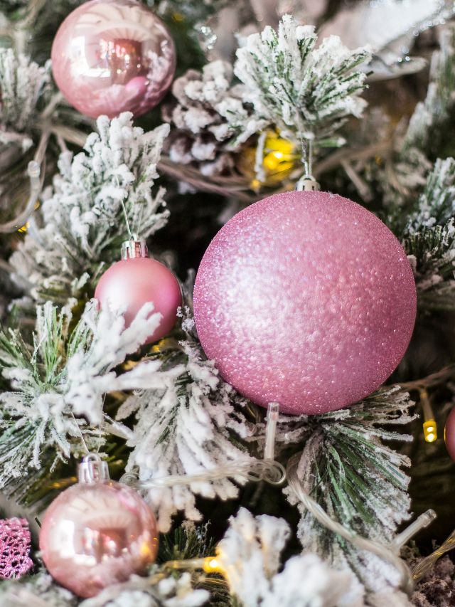 Pink christmas ornaments on a snowy christmas tree.