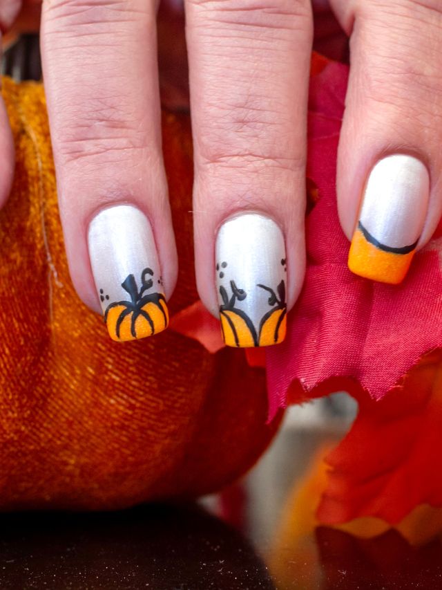 A woman's hand holding a pumpkin nail art design.