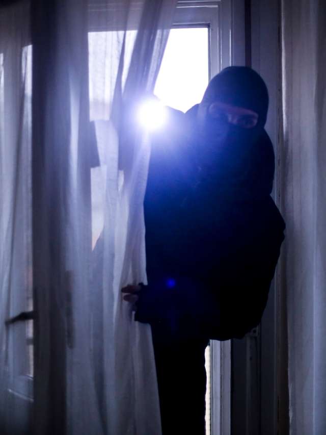 A thief in a black hoodie standing in front of a window.