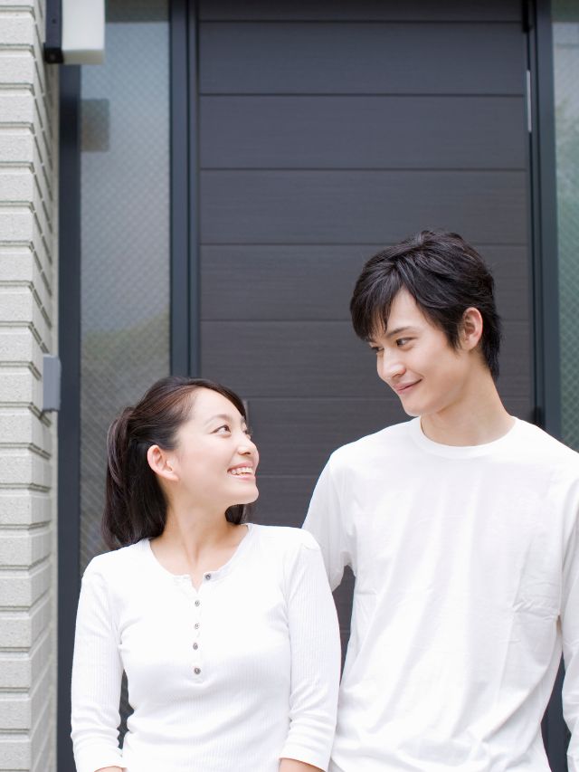 A young asian couple standing in front of their home.