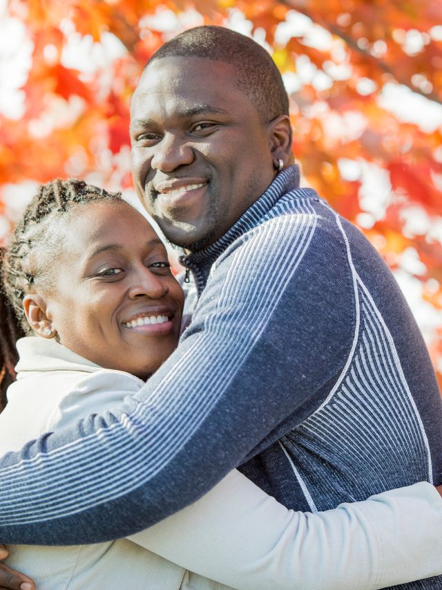 An african-american couple embracing in front of a fall tree.