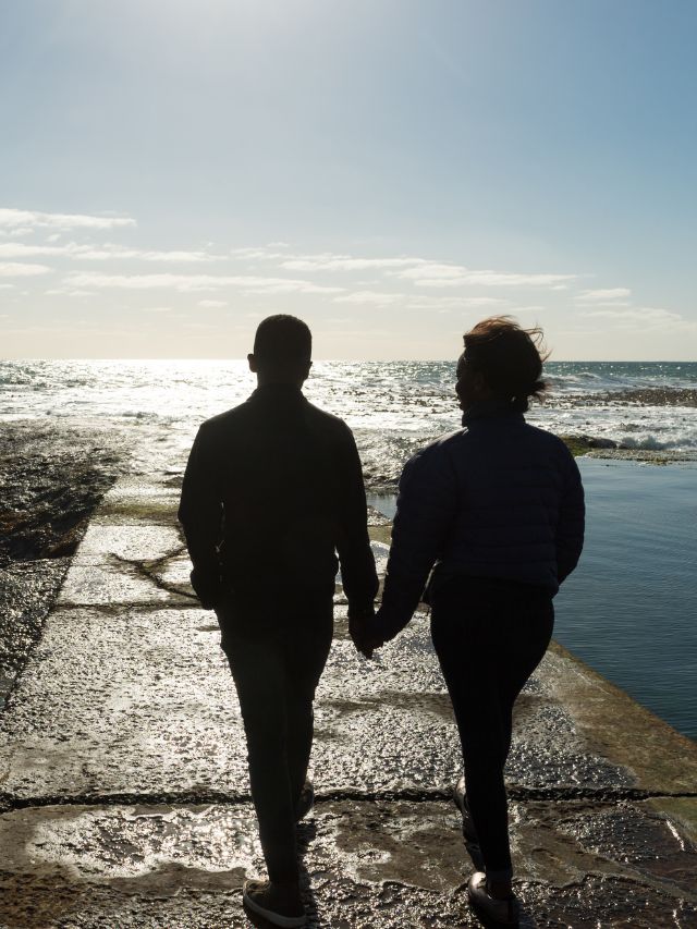 A couple holding hands on a pier in front of the ocean.