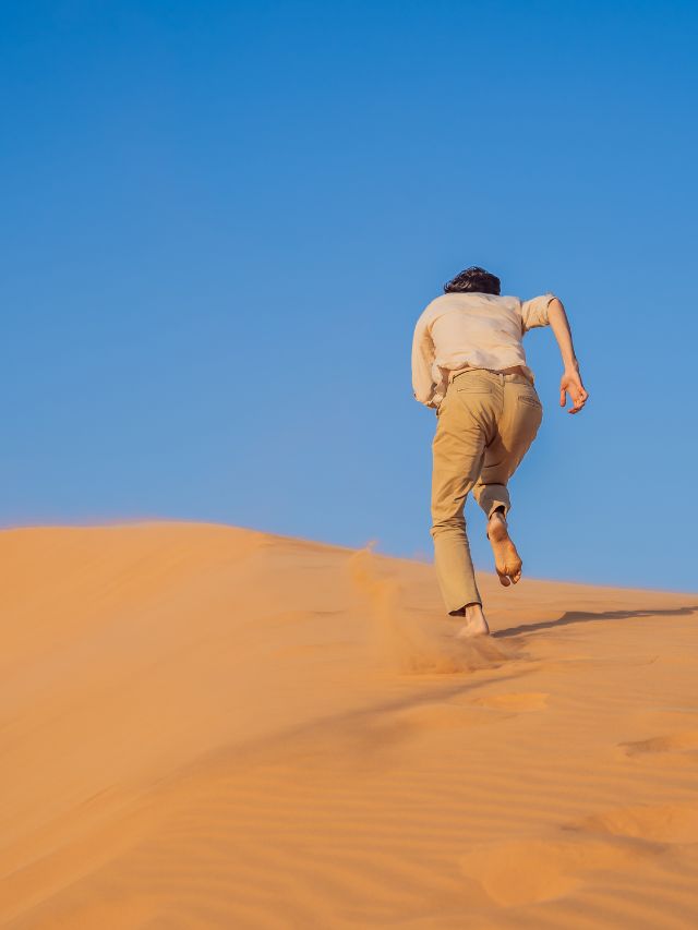 A man running on a sand dune in the desert.